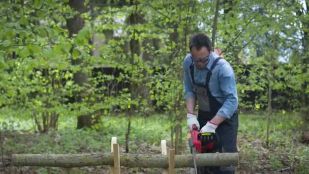 Lumberjack in workwear saws firewood on sawhorses with electric saw. Forest. — Stock Video