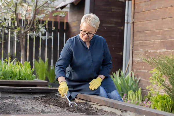 Hermosa jardinera femenina elimina las malas hierbas del jardín con azada, cultivando tierra — Foto de Stock