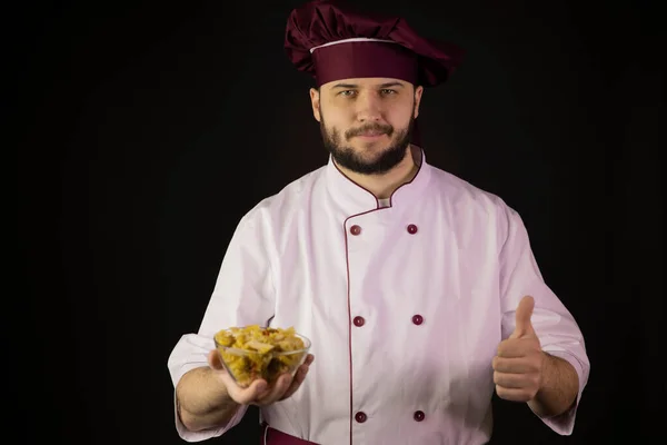 Glimlachende chef-kok in uniform houdt kom met verschillende droge pasta tonen als teken — Stockfoto