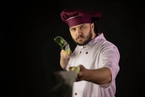 Handsome chef man in uniform directs leek stalks into camera like sword weapon