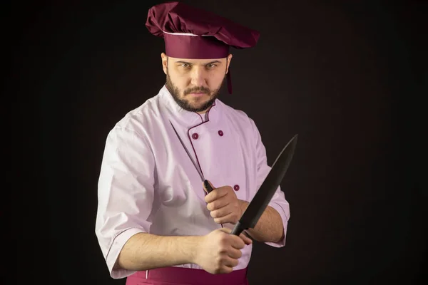 Hombre de chef agresivo en uniforme sostiene dos cuchillos cruzándolos como peleando —  Fotos de Stock