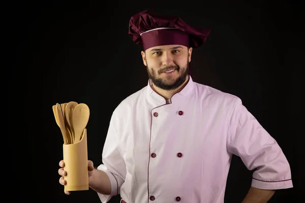 Sonriente guapo chef hombre en uniforme sostiene utensilios de cocina de madera utencils —  Fotos de Stock