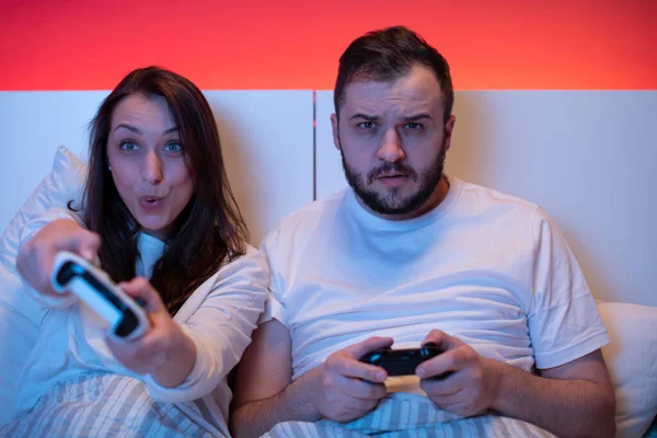 Beau jeune couple s'amuser à la maison, joue à des jeux vidéo avec des joysticks au lit — Photo