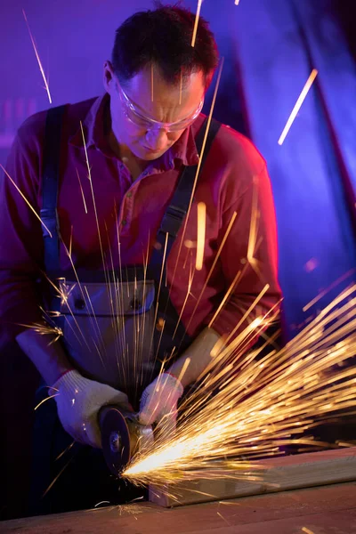 Hombre en gafas de mono y guantes moliendo metal con chispas en luz de color — Foto de Stock