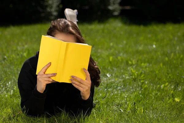 long hair brunette lying on grass of green lawn reading yellow book