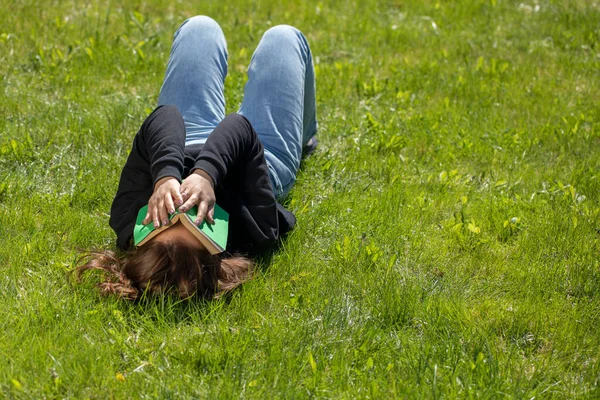 long hair brunette lying on grass of green lawn covering her face with book