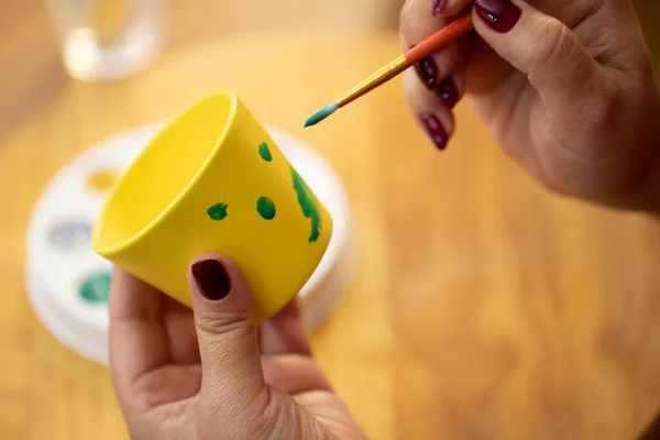 Pasatiempo de dibujar las manos de las mujeres pintando maceta amarilla con pinturas verdes — Foto de Stock