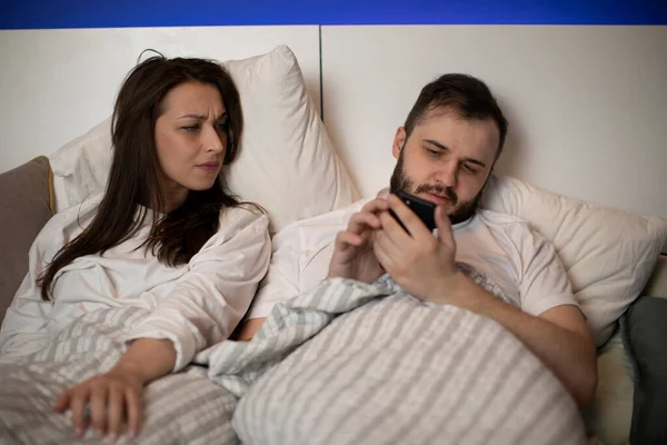 Man checks social network in bed ignoring wife, girl looks displeased at screen