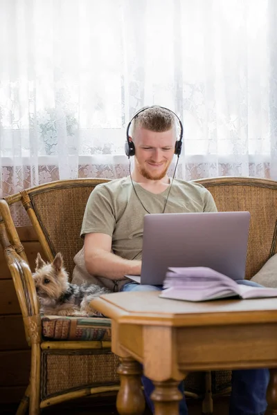 Sonriente joven en los auriculares funciona con el ordenador portátil en la casa de campo — Foto de Stock