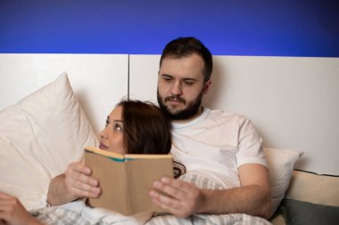 Yatakta uzanmış kitap okuyarak vakit geçiren güzel genç bir çift.