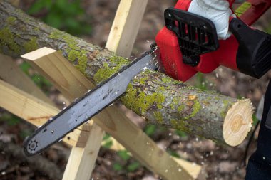 Testereyle odun kesen bir adam, testereyi yakın çekimde kullanıyor.