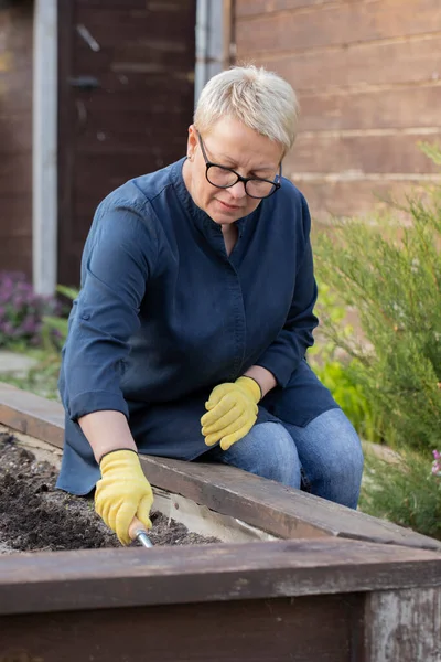 Mujer jardinero afloja tierra en macizo de flores para plantar plantas en su jardín — Foto de Stock