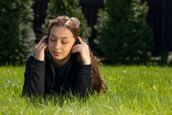 Pretty long hair brunette lying on green lawn listening music with headphones