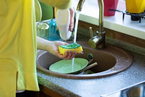 casually dressed girl washes dishes under jet of water in country house close up