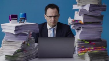 Yoğunlaşmış ofis çalışanı iş adamı bir yığın evrak işi arasında dizüstü bilgisayarda çalışır.