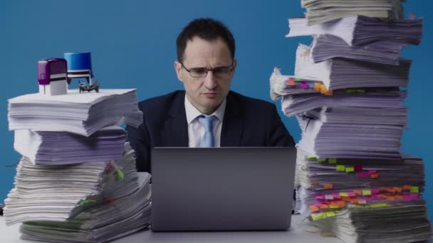 Serieuze manager werkt op laptop tussen stapels papierwerk, overladen met werk — Stockvideo