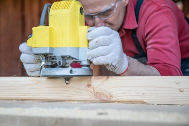 Sanatçı, kulübe atölyesinde değirmencilik aracıyla ahşap atölyede çalışıyor.