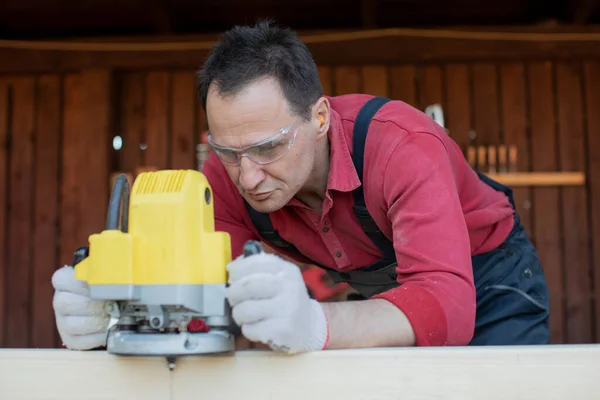 Artigiano lavora su trave di legno con strumento di fresatura da vicino al laboratorio cottage — Foto Stock