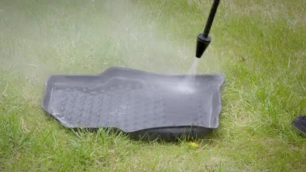 Man washes a rubber mat from a car on a lawn using a high pressure washer — Stock Video
