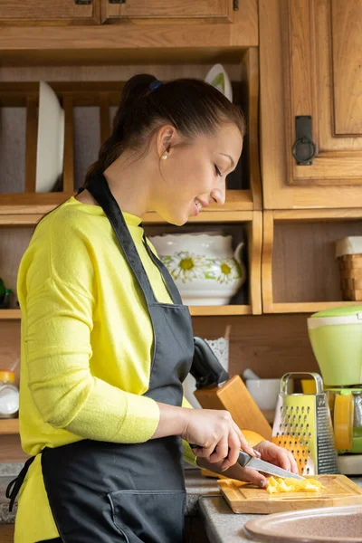 Smiling housewife slices vegetables on wooden board in reallife kitchen interior