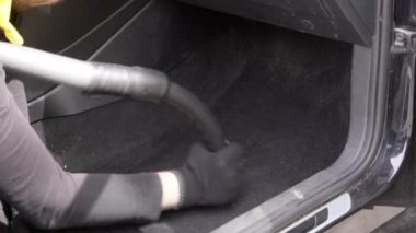 Kirli bir arabanın içini elektrikli süpürgeyle süpüren bir erkek işçi..