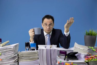 Ofiste kağıt yığınıyla masada oturan çok çalışan bir adam.