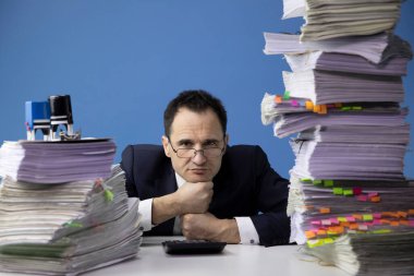 Yorgun bir ofis çalışanı kafasını bir yığın belgenin arasına koyar.