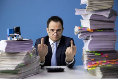 tired office worker Make a fuck sign sitting at desk with huge pile of documents