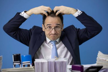 İş stresindeki kameraya bakarak başını kaşıyan yorgun bir ofis çalışanı.
