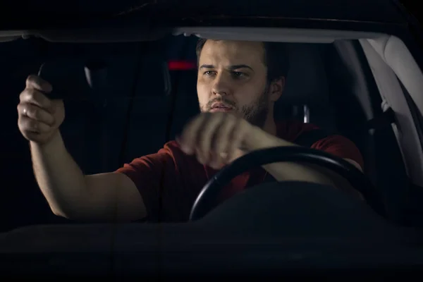 Conductor masculino se sienta al volante del coche por la noche ajustando el espejo retrovisor — Foto de Stock