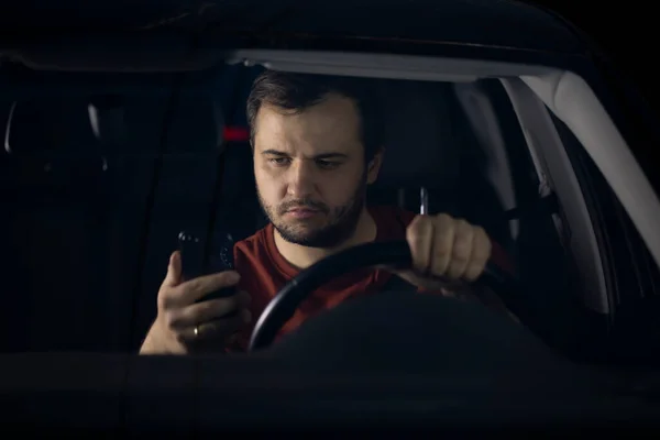 Triste conductor se sienta en el coche por la noche cansado mirando teléfono inteligente preocupado por los problemas — Foto de Stock