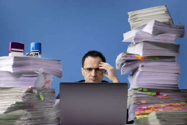 Офисный работник завален документами, работающими сверхурочно на ноутбуке — стоковое фото