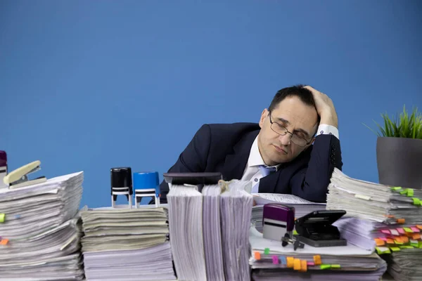 Перегруженный работой бизнесмен спит за рабочим столом, полным бумажной работы. — стоковое фото