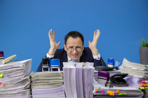stressed and overworked businessman yelling in office with huge stack documents