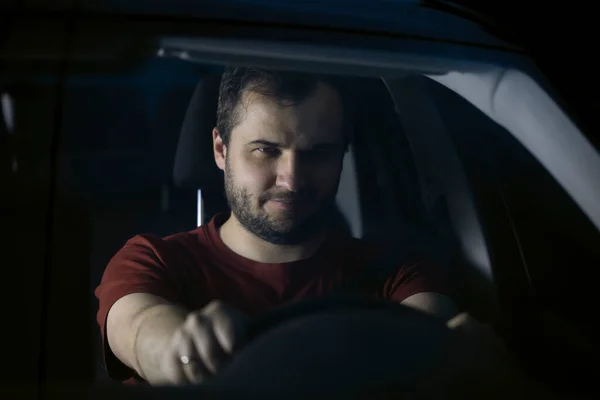 Sonriente hombre conductor se sienta en el coche por la noche pensativamente mirando hacia el futuro — Foto de Stock