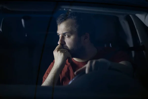 悲しい男の運転手は夜に車のハンドルに座って思慮深く離れて見て — ストック写真