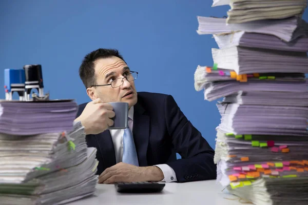 Empleado de oficina hecha polvo se ve asustado por la alta pila de documentos — Foto de Stock