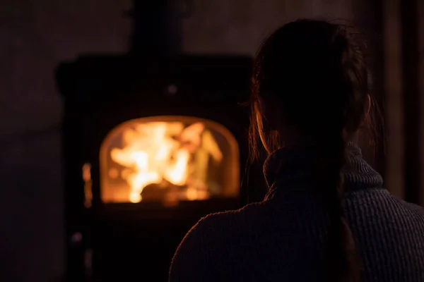 Vue arrière de la fille en pull gris regardant cheminée dans une chambre sombre confortable. — Photo