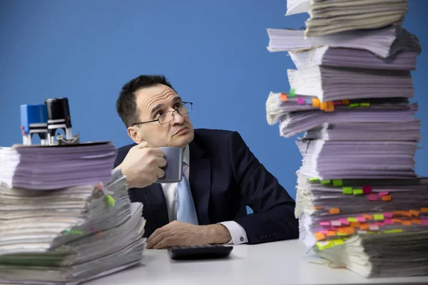Empresário exausto olha para grande pilha de documentos. demasiada papelada — Fotografia de Stock