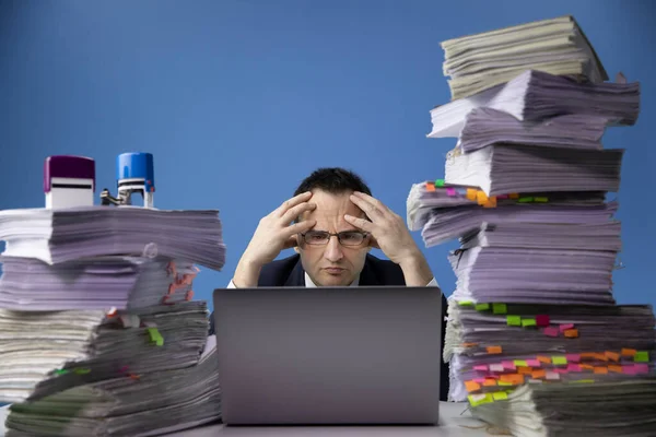 Moe bezorgde zakenman zit aan het bureau met enorme stapel documenten — Stockfoto