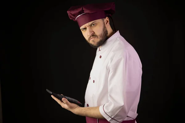 Verward chef-kok man houdt rekenmachine verdacht kijkt naar camera breakeven — Stockfoto