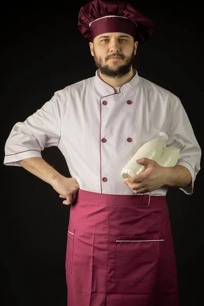 Guapo barbudo chef hombre en uniforme sostiene dos botellas con leche —  Fotos de Stock