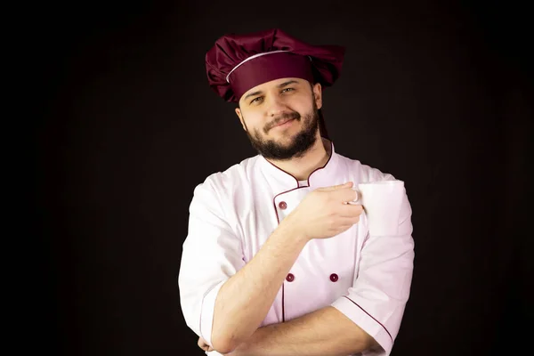 Joven hombre de chef barbudo feliz en uniforme sostiene taza de café de té y sonrisa —  Fotos de Stock