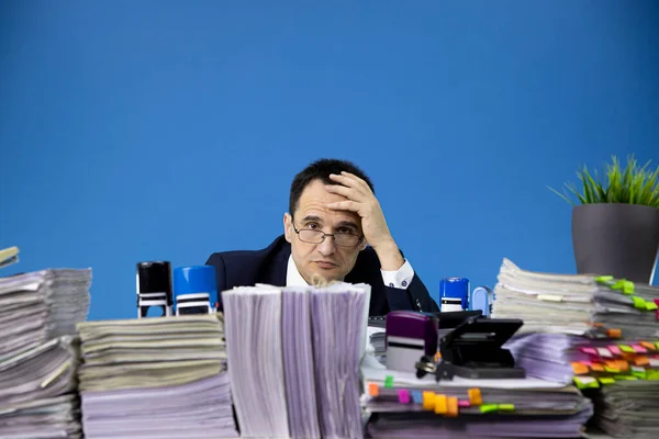 Agotado cansado hombre de negocios sobrecargado de trabajo se ve fuera de enorme pila de documentos — Foto de Stock