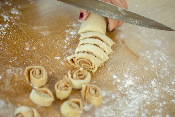 womens hands slice with knife cinnamon dough roll for homemade baking