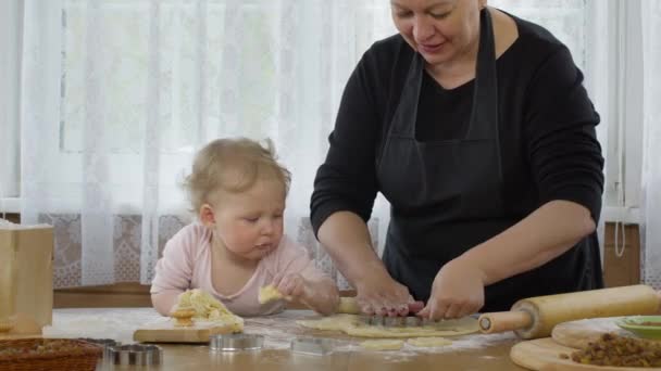 Babička krájí sušenky ze syrového perníkového těsta a vnučka ochutnává těsto. — Stock video