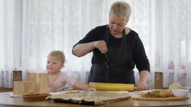 Niedliche Baby-Enkelin hilft Oma beim Mischen von Teig für Gebäck und legt Mehl — Stockvideo