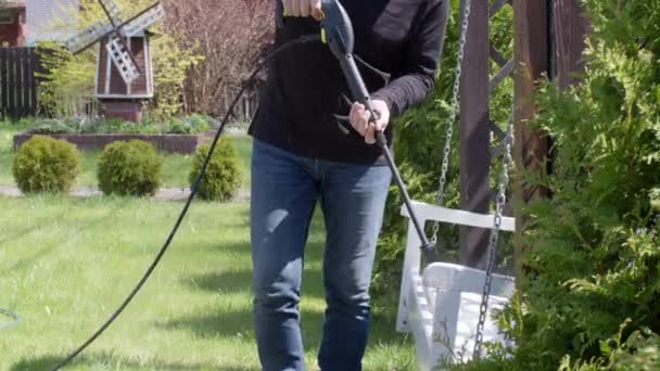 Caucasian man disinfects a bench hanging on chains with a high pressure washer — Stock Video