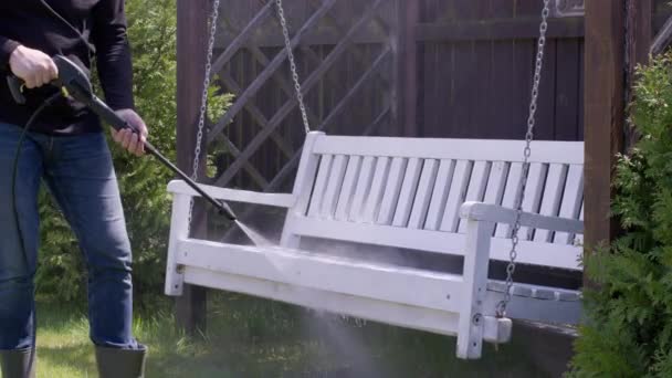 Kafkasyalı bir adam yüksek basınçlı çamaşır makinesiyle tahta bir bankta salıncaktaki kiri temizliyor. — Stok video