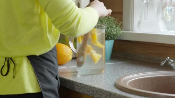 Jovem caucasiana menina mexe uma colher de madeira com limonada cítrica na cozinha — Vídeo de Stock